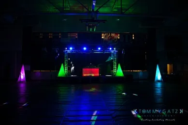 A dimly lit dance floor with colorful lights and illuminated triangular decorations, featuring a DJ booth in the center.