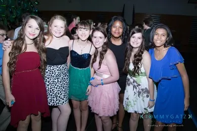 A group of seven young people in dresses posing together at a social event.