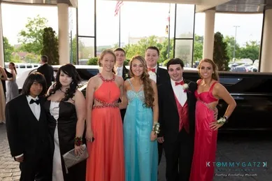 A group of young people dressed in formal attire, posing in front of a limousine.