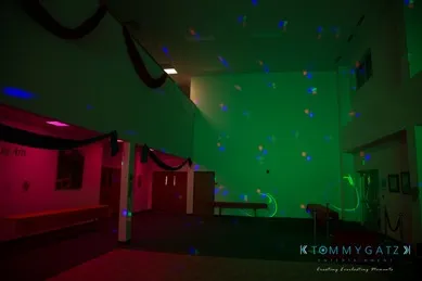 A dimly lit room with green and red lights on the walls and ceiling, decorated with black drapes.
