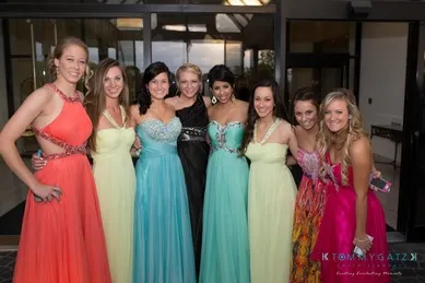 Seven people in formal dresses pose together in front of a building entrance.