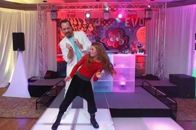 Man and girl dancing with colorful lights and event backdrop.