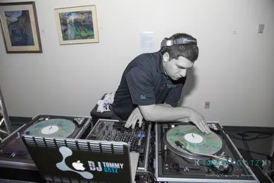 A DJ wearing headphones is mixing music on turntables in a room with framed artwork on the walls.