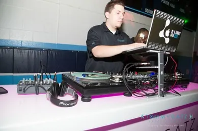 DJ using turntables and a laptop at a neon-lit setup, with headphones placed nearby.