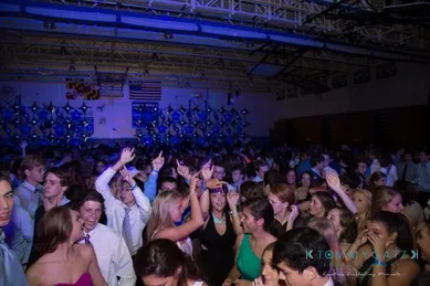 A crowded indoor party with people dancing and mingling under dim blue lighting and ceiling decorations.