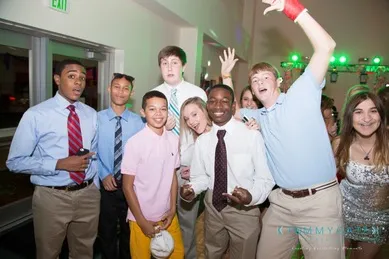 A group of teenagers in casual and semi-formal attire smiling and posing for a photo indoors at an event.