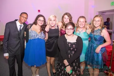 A group of seven people, dressed in formal attire, pose together in a brightly lit room.