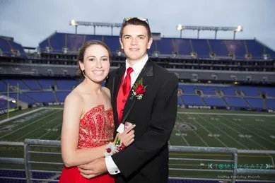 A young couple in formal attire stands together in a stadium overlooking the field.