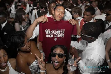 A group of students at a dance; one holds up a Broadneck High School shirt. Others pose with peace signs and wear sunglasses.