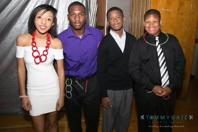 Four people dressed in formal attire stand together indoors, wearing colorful glow stick accessories.