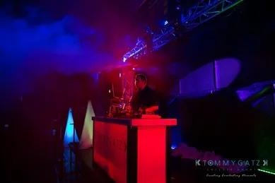 DJ performing on a dimly lit stage with vibrant red and blue lights.