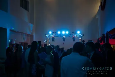 A dimly lit indoor party or event with people mingling and blue stage lights in the background.