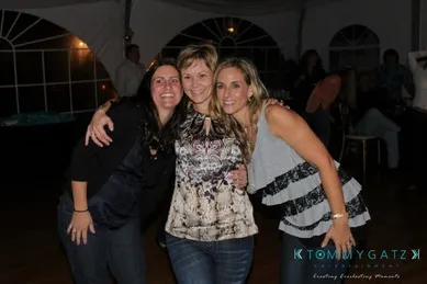 Three people smile and pose together at an indoor event with others in the background.