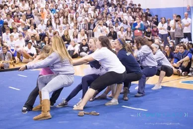 A group of women competes in a tug-of-war game inside a gymnasium, watched by a large audience.