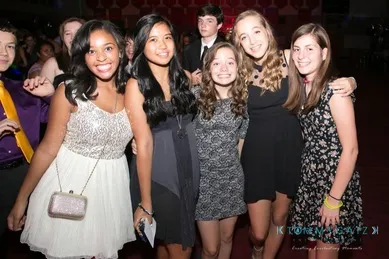 Group of five teens smiles for a photo at a social event. They are dressed in formal attire and stand closely together.