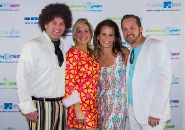 Four people in retro-themed outfits pose together, smiling in front of a branded backdrop.