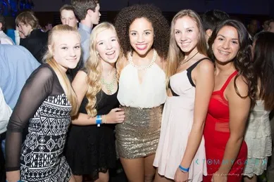 A group of five young people smiling at a party, dressed in semi-formal attire.