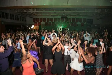 A large group of people on a dance floor clapping and raising their hands at a lively event in a gymnasium.