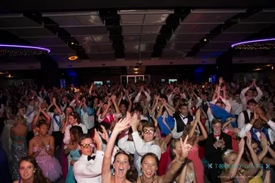 A large crowd of people in formal attire enthusiastically cheering and clapping in a dimly lit venue.
