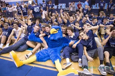 Group of students with a blue bird mascot pose on the gym floor during a school event.