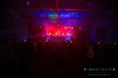 A crowd at a dark indoor concert with colorful stage lights and laser effects.