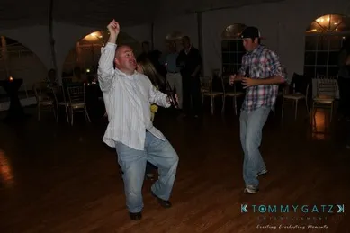 Two men dancing energetically in a dimly lit room with wooden floors and chairs in the background.
