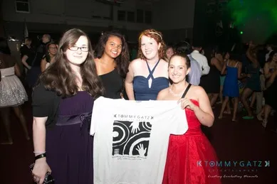 Four young women at a party, one holding a t-shirt with a graphic design.