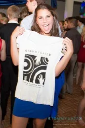A woman in a blue dress holds up a white T-shirt with a graphic design at a crowded event.