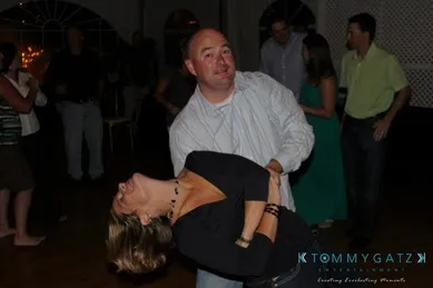 A man in a striped shirt dips a smiling woman on a dance floor, surrounded by other people.