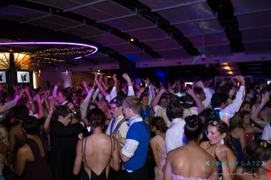 A crowded dance floor at a party, with attendees in formal attire dancing energetically under colorful lights.