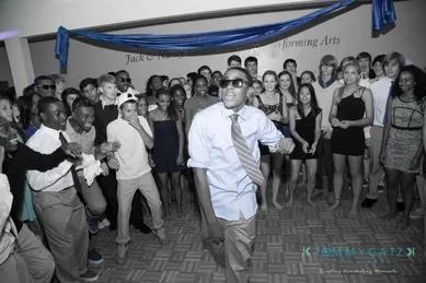 A person dancing energetically in front of a crowd at a party, with blue accents highlighting the scene.