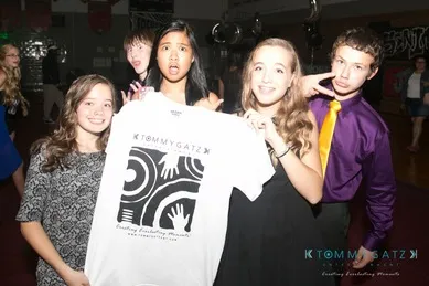 Group of young people at an event, with one holding a Tommy Gatz t-shirt, posing for a photo.