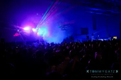 A crowd at a concert or party with colorful lights and fog.