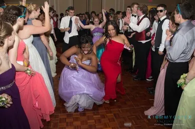 People dancing energetically at a formal event wearing colorful dresses and suits.