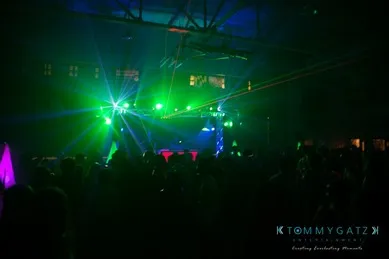 A dimly lit indoor concert with green and blue stage lights illuminating the crowd and ceiling.