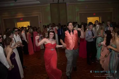 A couple dressed in formal attire dances in the center of a crowded ballroom at an event.