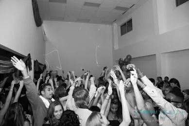 Black and white photo of a crowded indoor party, people raising their hands and cheering.