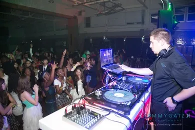 DJ performing at a party with a crowd dancing and cheering in a dimly lit venue.