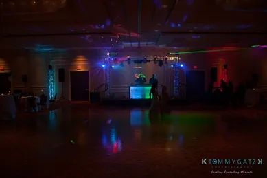 Dimly lit room with colorful stage lights, a DJ booth in the background, and few people on the dance floor.