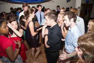 A group of people dancing and interacting on a crowded dance floor at an indoor event.