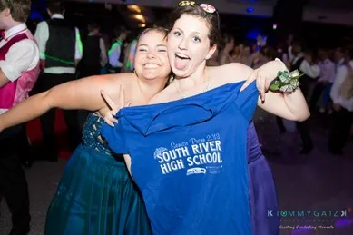 Two people at a prom event smiling, with one holding a "South River High School" T-shirt.