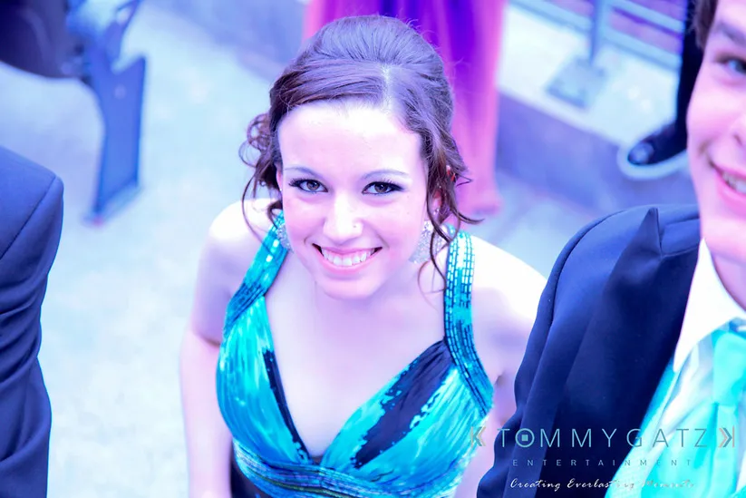 Person in a blue dress smiling at the camera, standing next to others in formal attire.