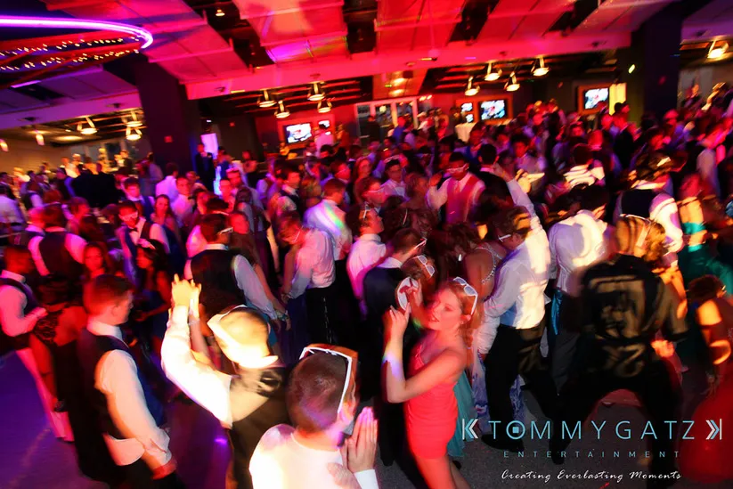 A large group of people dancing in a dimly lit room with colorful lights.