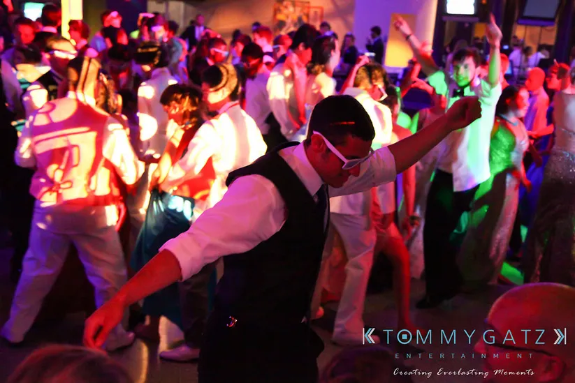 A crowd of people dance energetically under colorful lights at a lively party.