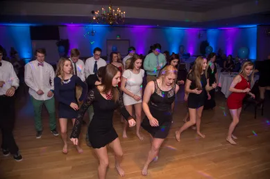A group of people are dancing in a dimly lit room with colorful lights.
