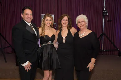 Four people dressed formally pose together in front of a purple curtain.