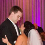 A bride and groom share a dance at their wedding, with purple drapery in the background.