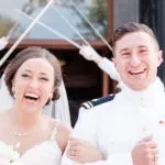 A bride and groom in uniform walk joyfully past a military saber arch.