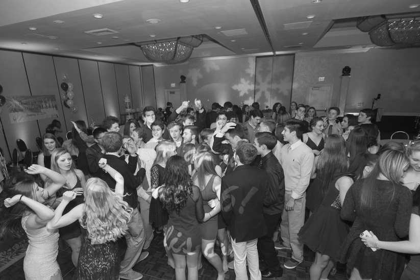 A large group of young people dancing in a dimly lit room with balloons and streamers decorating the space.