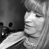 A black and white photo of a person with long hair looking down, wearing a pearl necklace.